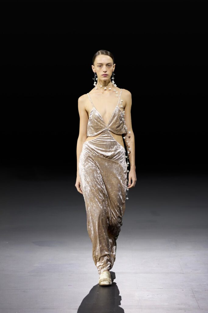 A fitted beige velvet sleeveless dress with a deep neckline and elegant draping.