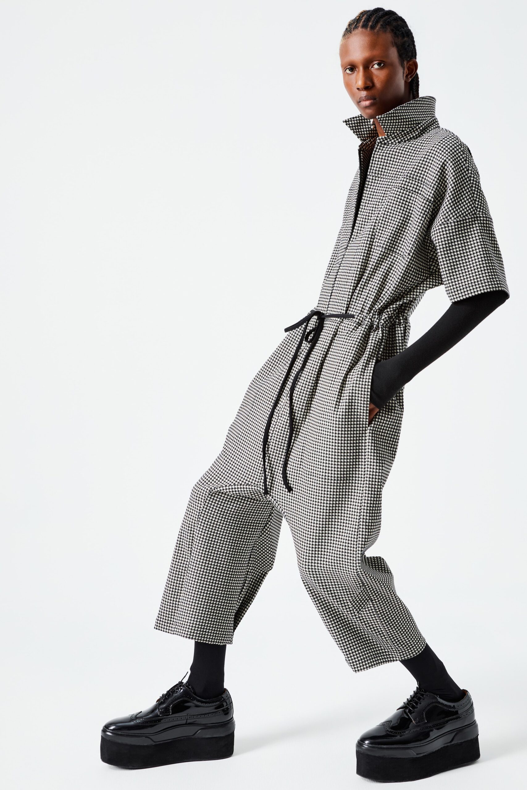 This relaxed jumpsuit features a striking black and white check pattern, enhanced by a belted waist that defines the silhouette. The short sleeves and collared neckline add a contemporary edge, creating a modern look that is both functional and stylish.