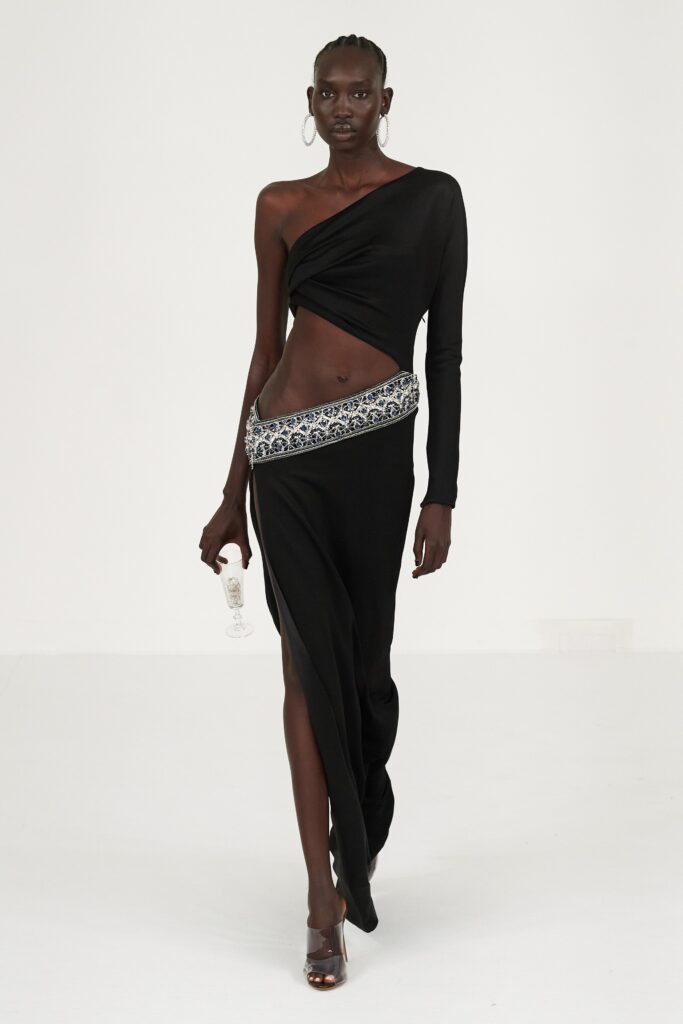 A fitted black silk dress with long sleeves, an asymmetric design, and a stylish slit.