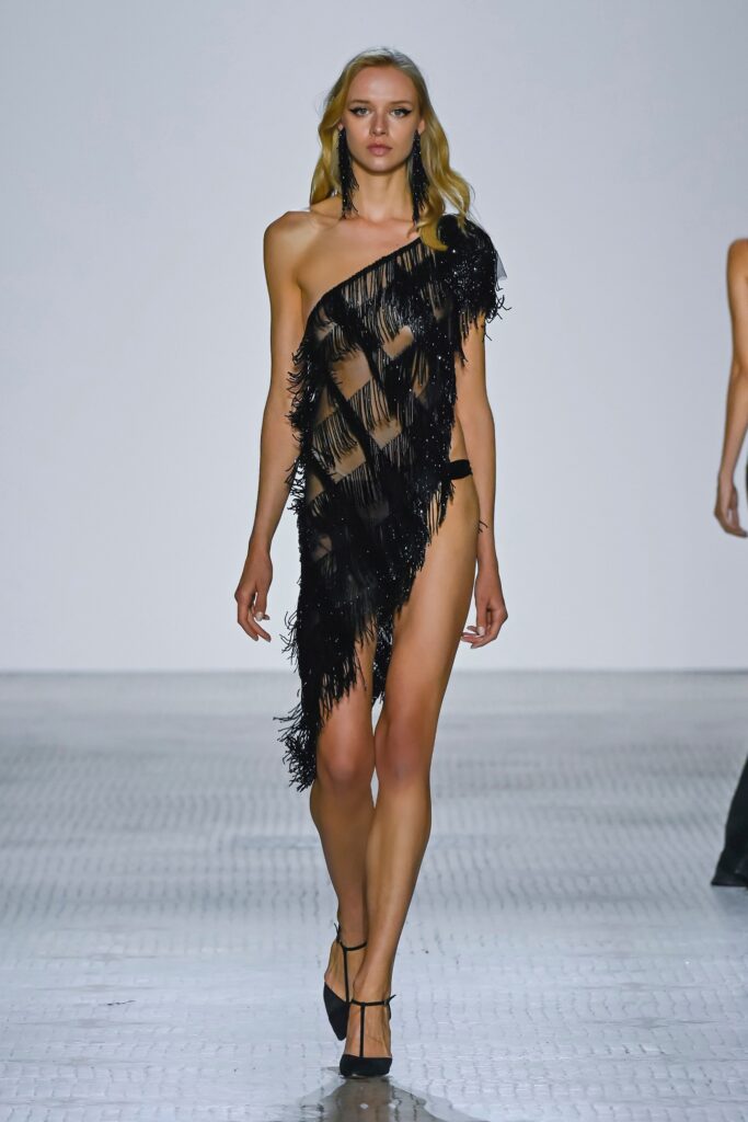 A fitted black silk sleeveless dress with an asymmetric design and fringed detailing.