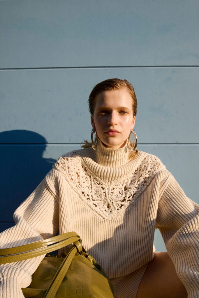 An oversized beige cotton sweater with long sleeves and an embroidered turtleneck design.