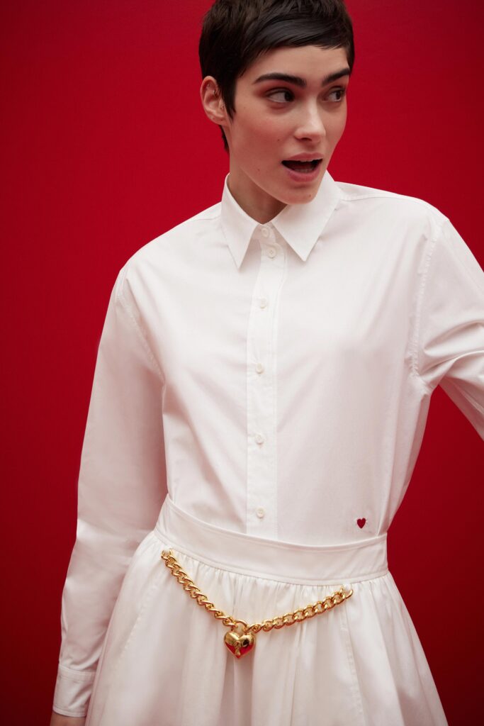 A fitted white shirt-dress with long sleeves, a collared neckline, and pleated detailing.