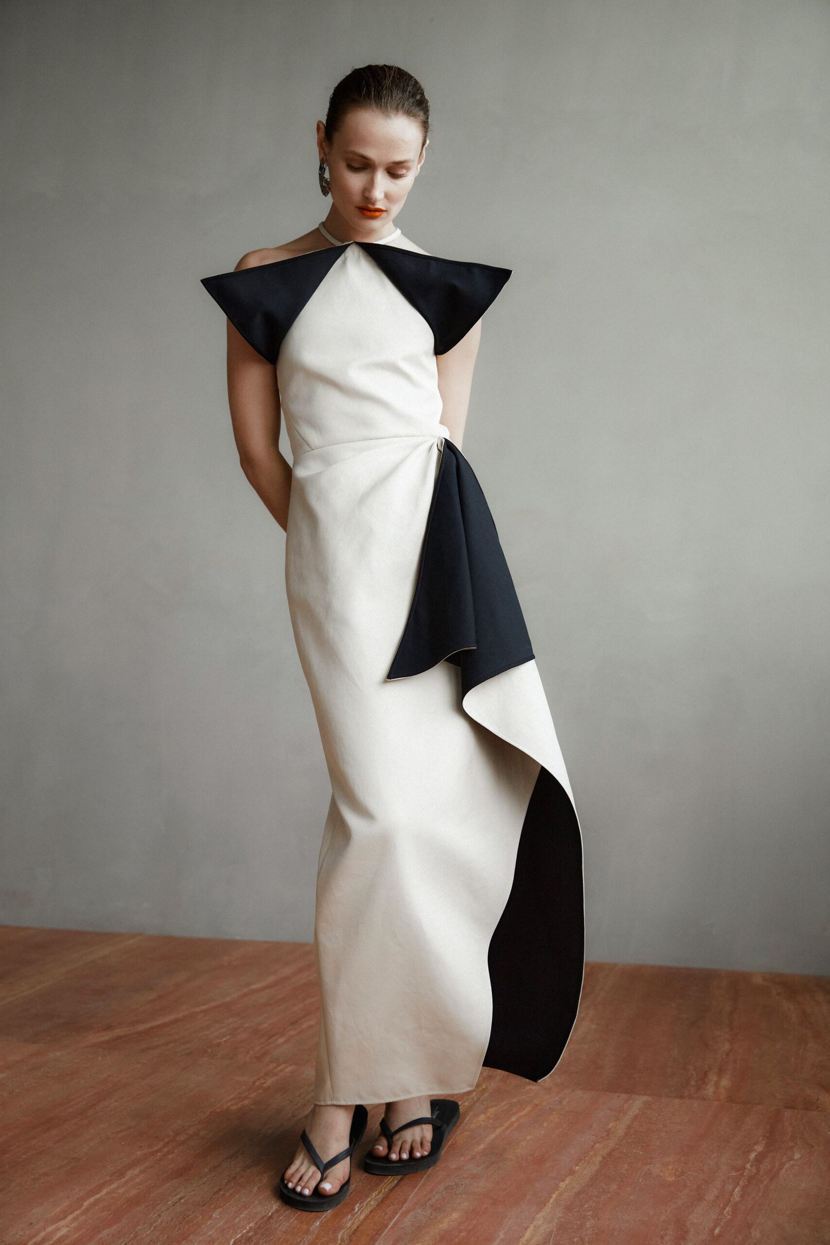 A fitted black and white sleeveless dress with a high neckline and asymmetric draped design.