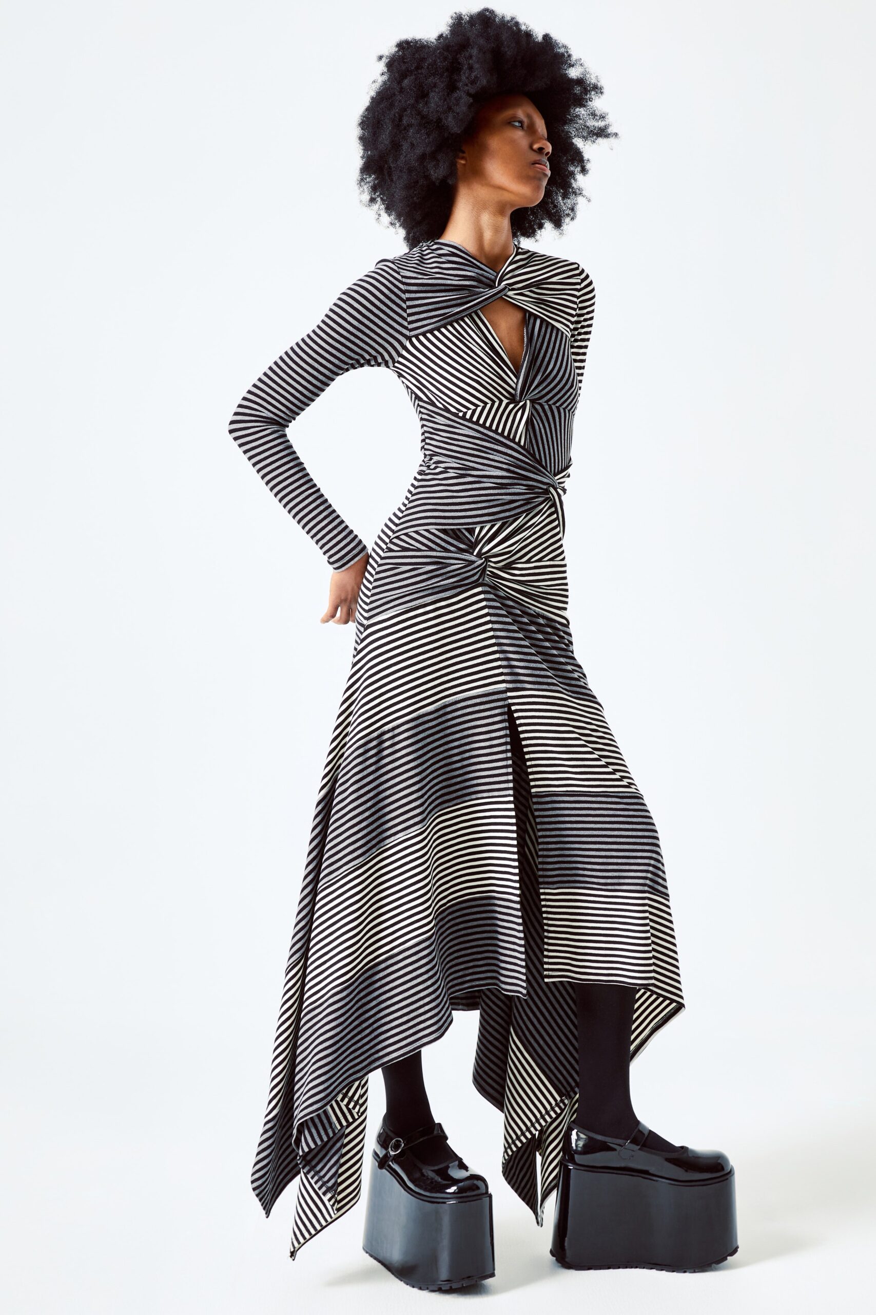 This fitted dress features a striking asymmetric silhouette, enhanced by bold black and white stripes that create a dynamic visual rhythm. The deep V-neckline adds a touch of sophistication, while the long sleeves provide a balanced contrast to the flowing hemline.