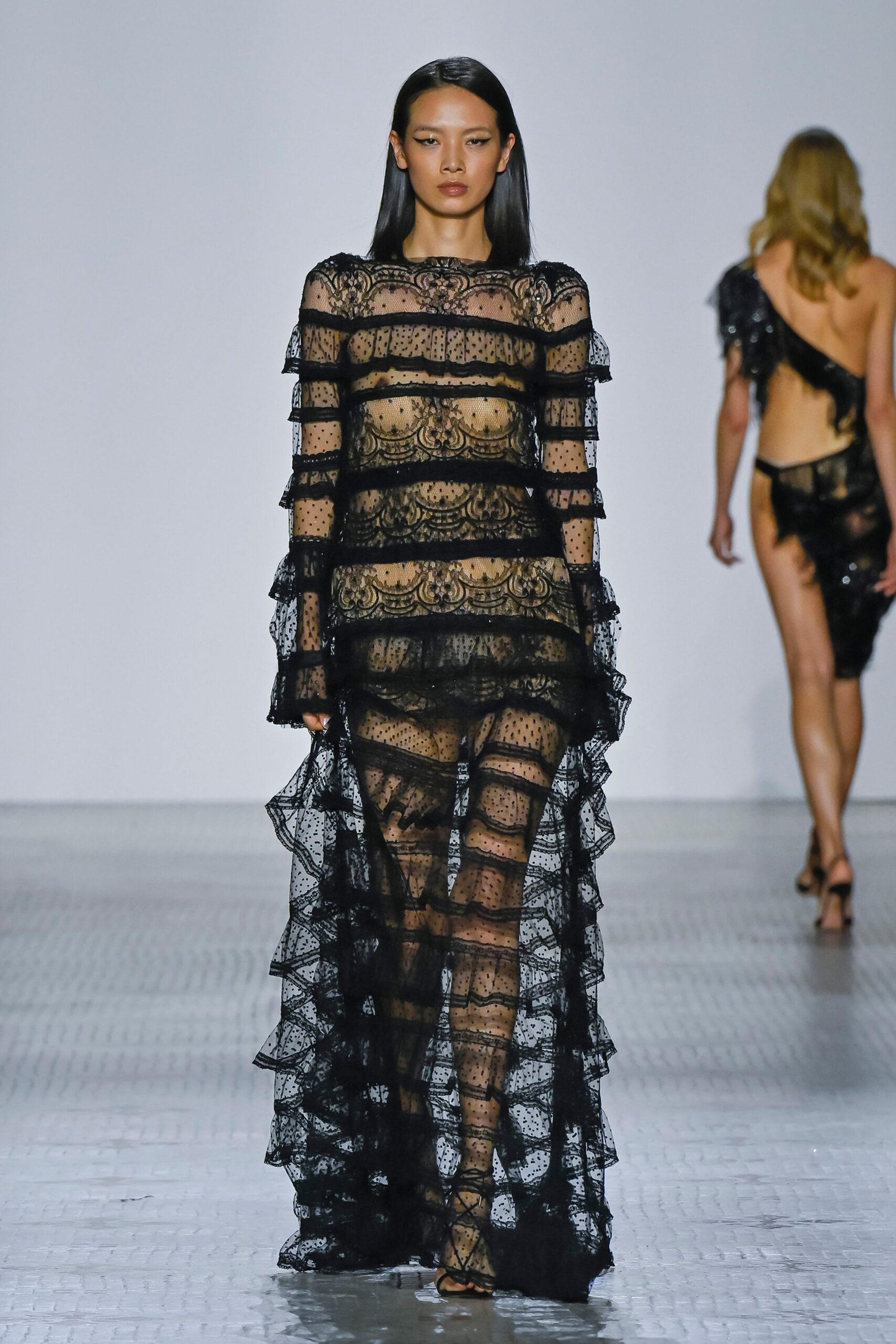 A fitted black lace dress with long sleeves, a V-neckline, and tiered design details.