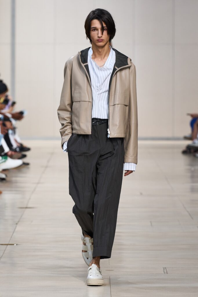 A relaxed beige leather jacket paired with striped long-sleeve shirt and wide-leg gray pants.