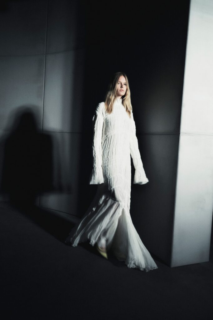 A fitted white silk dress with long sleeves and a tiered silhouette.