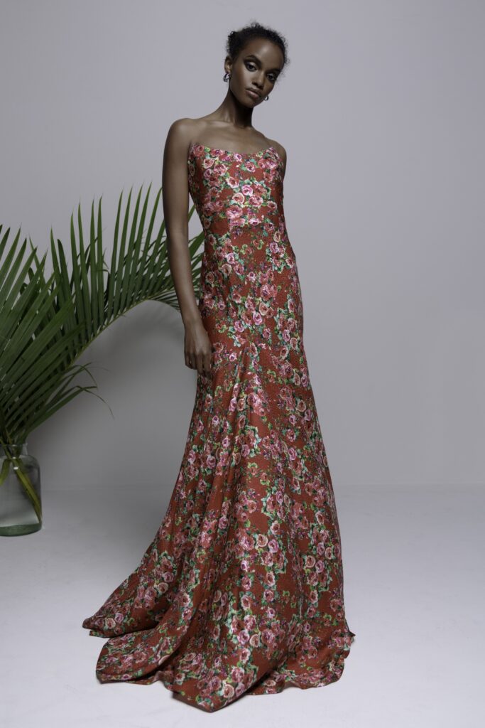 A fitted red silk gown with a strapless design and flared silhouette, adorned with floral patterns.