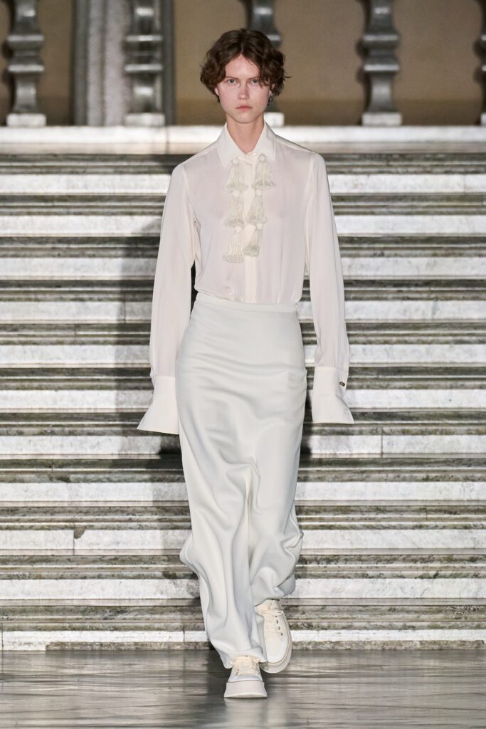 A fitted white silk long-sleeve shirt with pleated details paired with a matching skirt.
