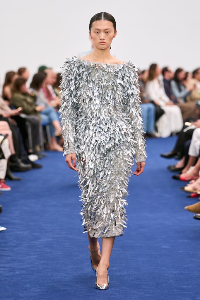 A fitted silver dress with long sleeves and an off-shoulder design, featuring a fringed texture.