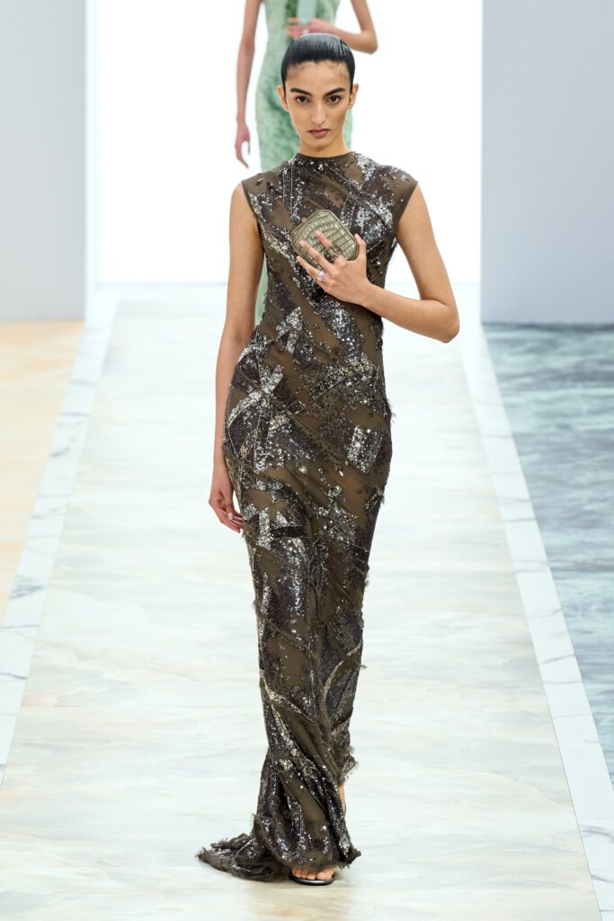 A fitted green silk gown with a sleeveless design, high neckline, and sequined detailing.