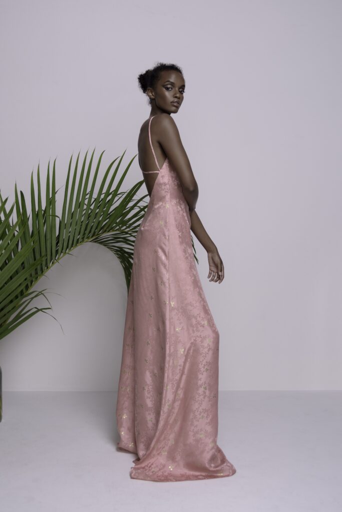 A fitted pink silk maxi dress with a sleeveless design and V-neckline.