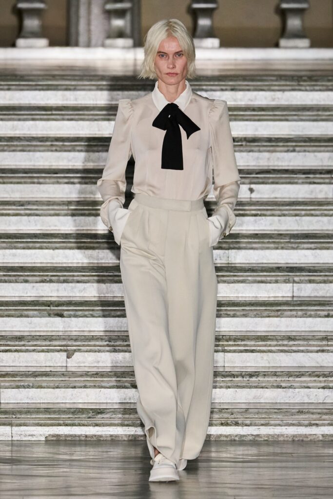 A fitted white blouse with long sleeves and a collar, paired with high-waisted pants.