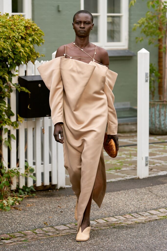 A relaxed beige silk off-shoulder dress with long sleeves and an asymmetric design.
