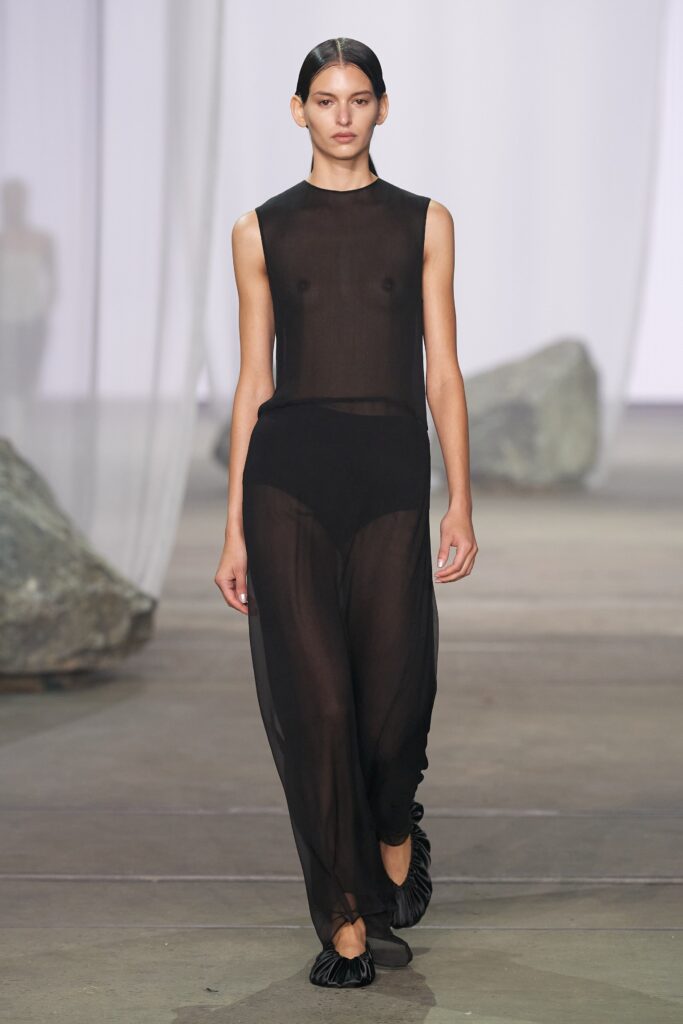 A fitted black sheer dress with a high neckline and asymmetric design detail.