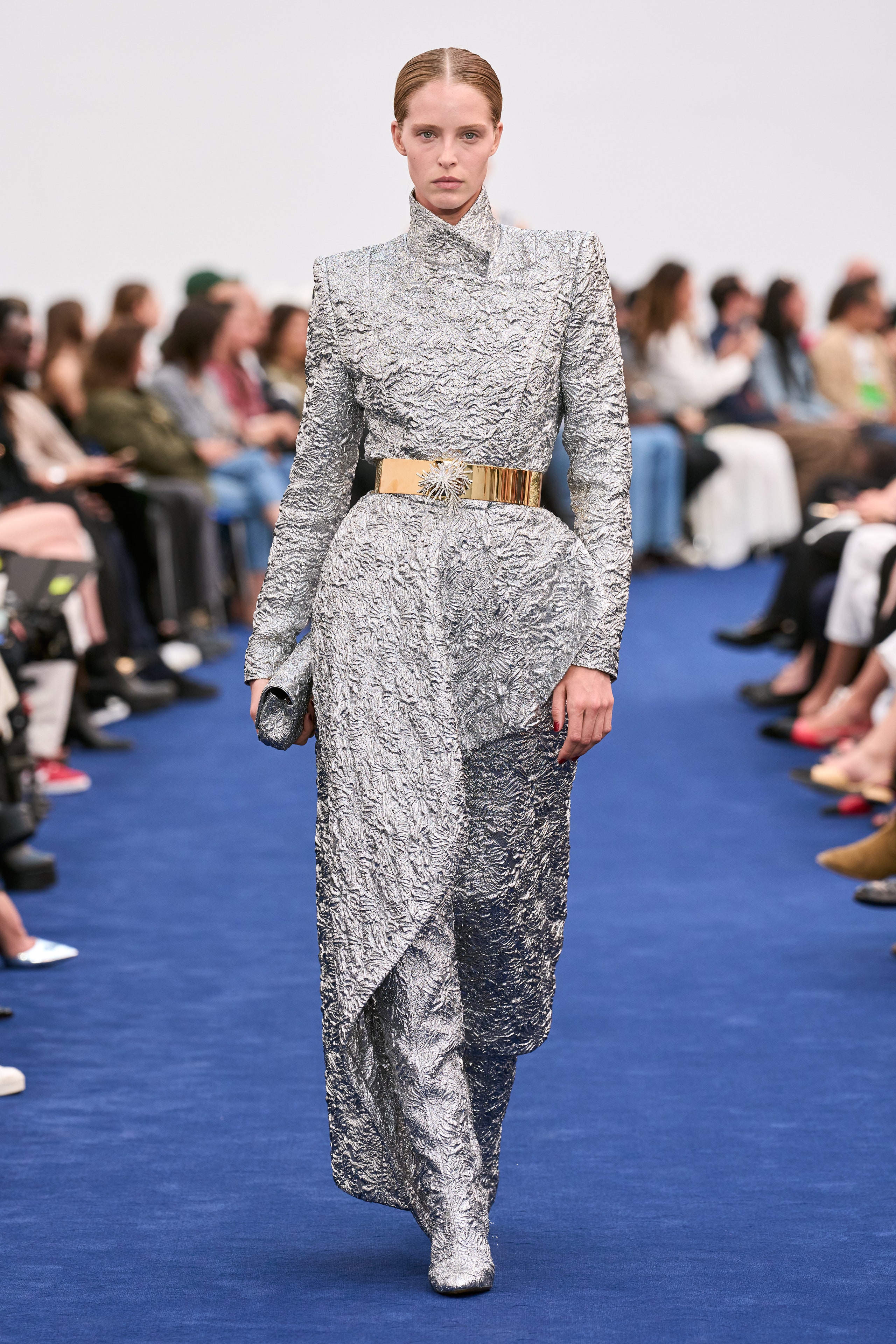 A fitted silver metallic dress with long sleeves, high neckline, and an asymmetric design.