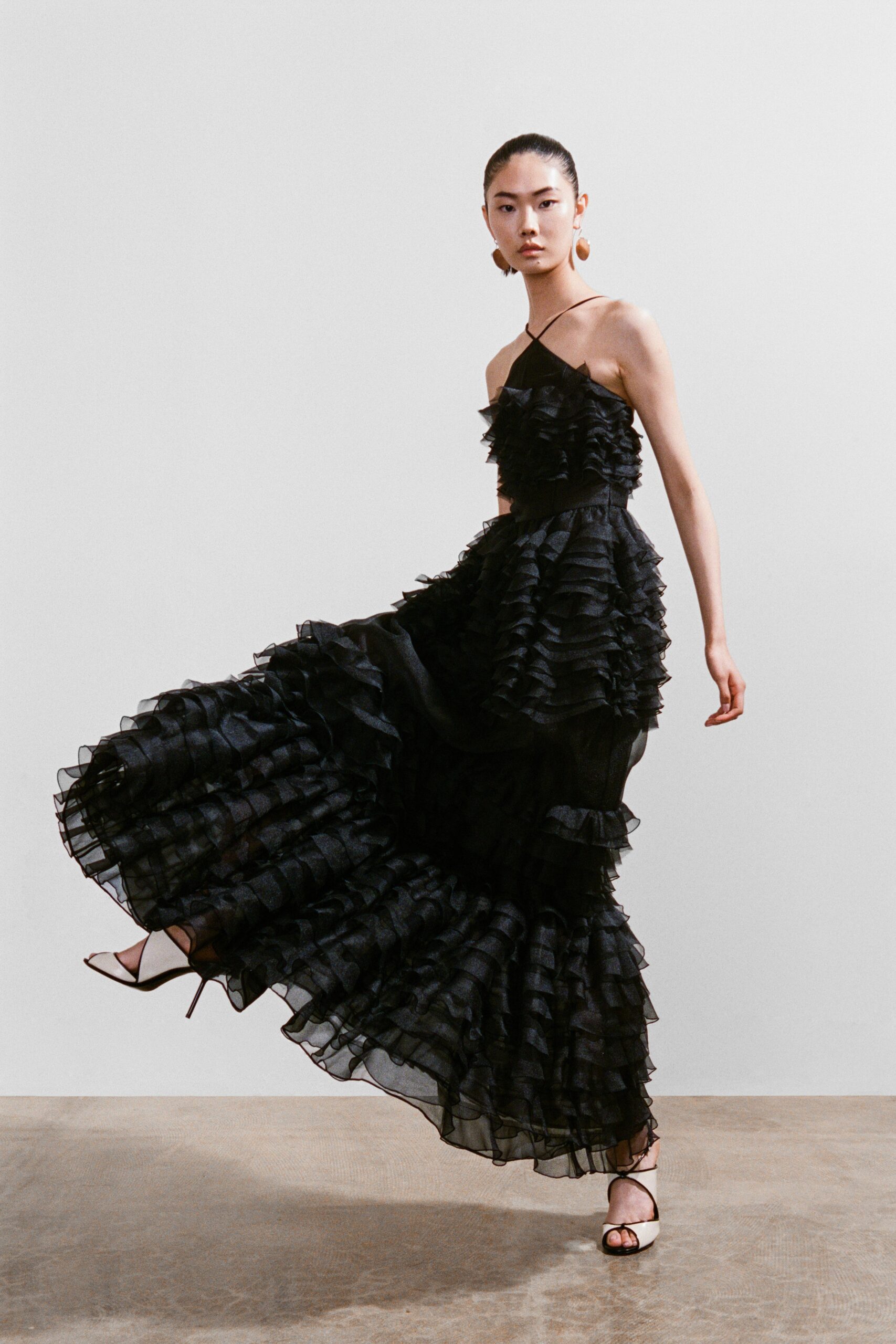 A fitted black silk sleeveless dress featuring a V-neckline and ruffled, tiered design.