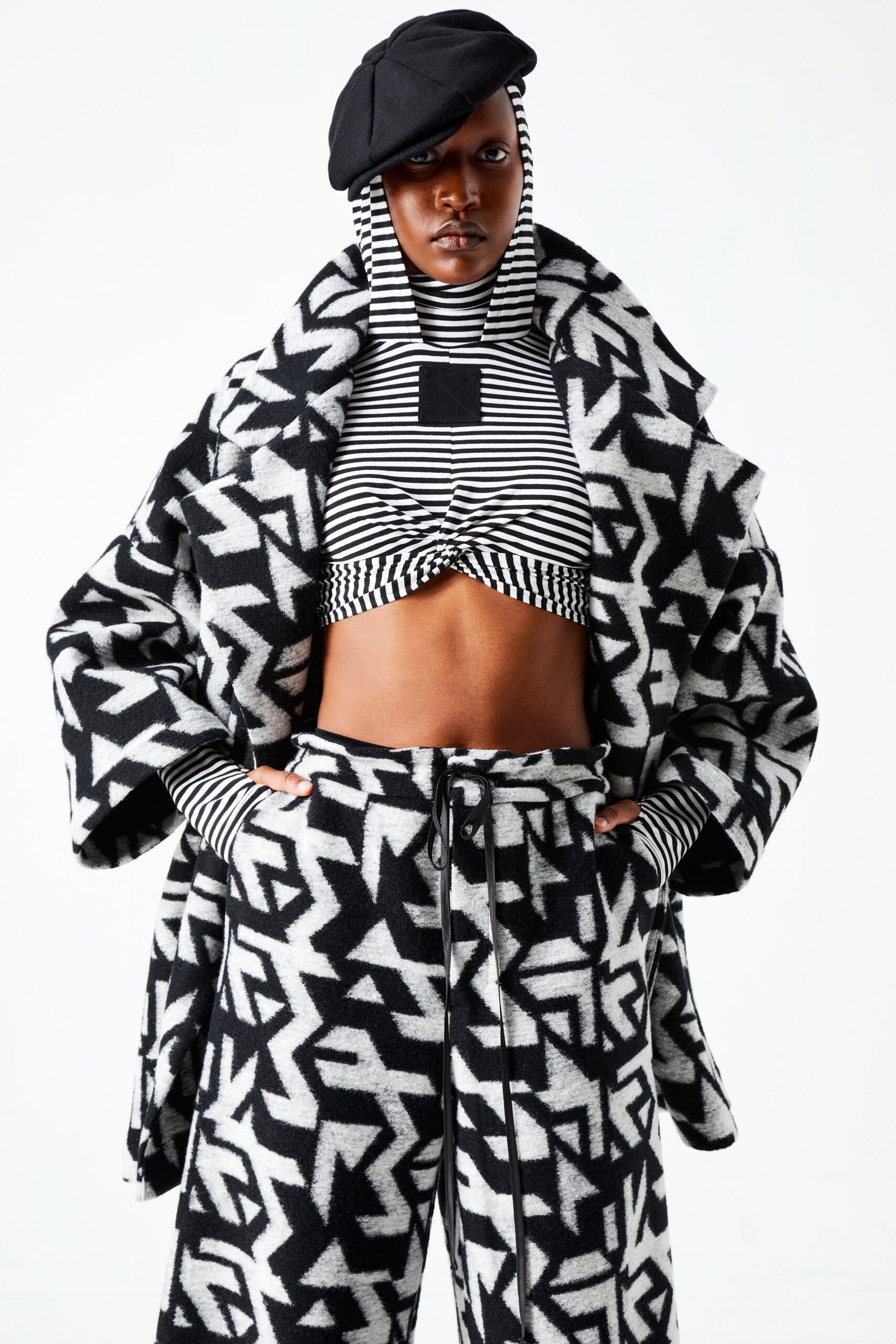 This relaxed coat features a striking black and white geometric print, creating a bold visual statement. The layered look is complemented by a cropped top underneath, adding depth and contrast to the ensemble.