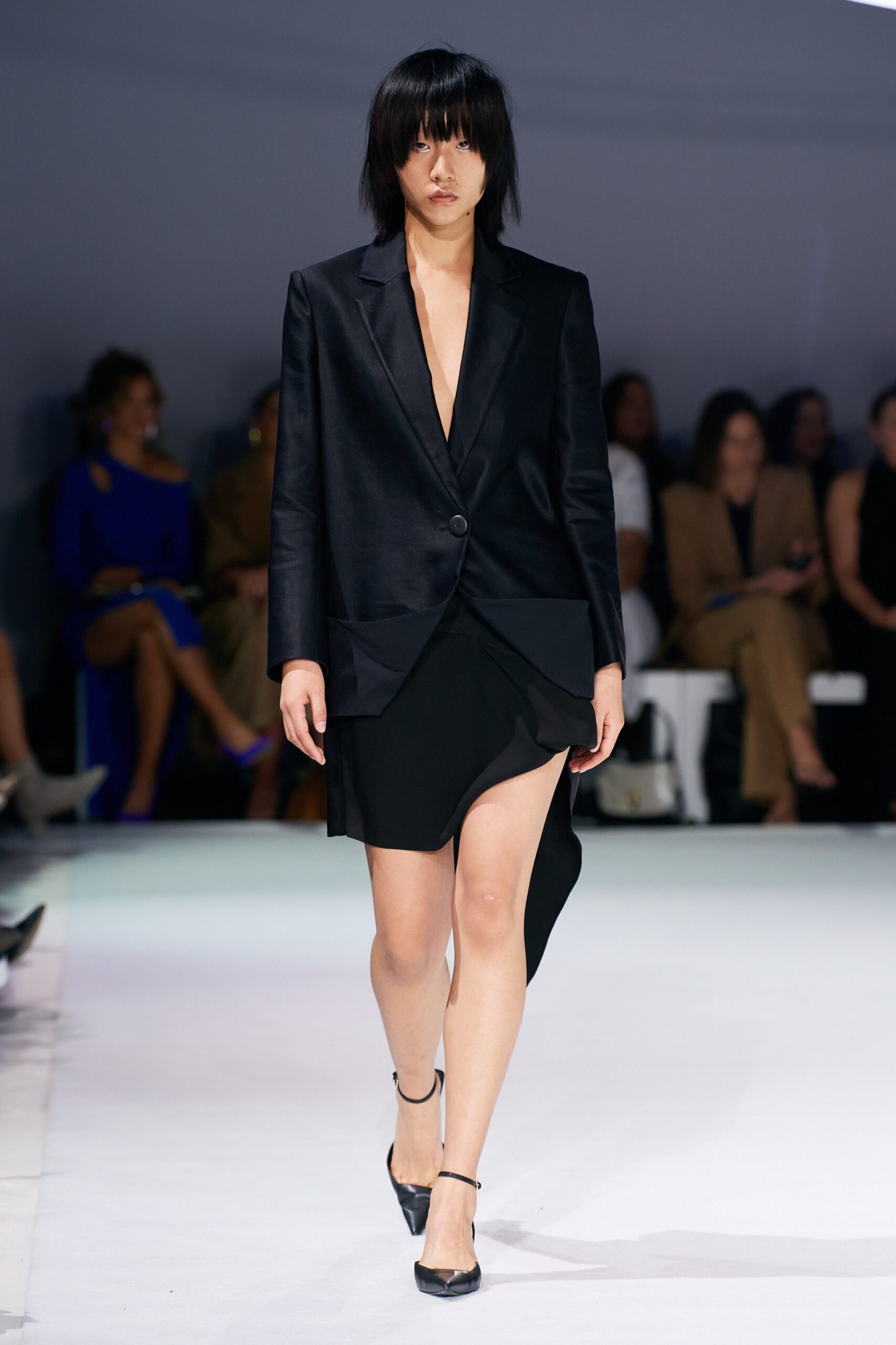 A fitted black silk blazer dress with a V-neckline and asymmetric slit detail.