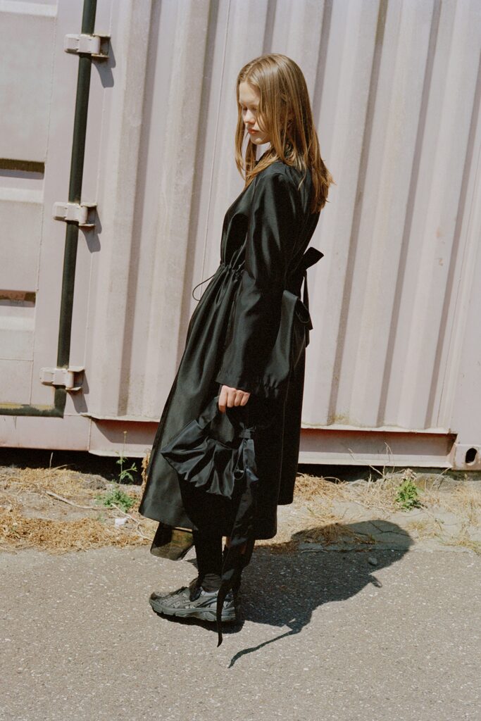 A fitted black silk dress with a V-neckline and asymmetric design details.