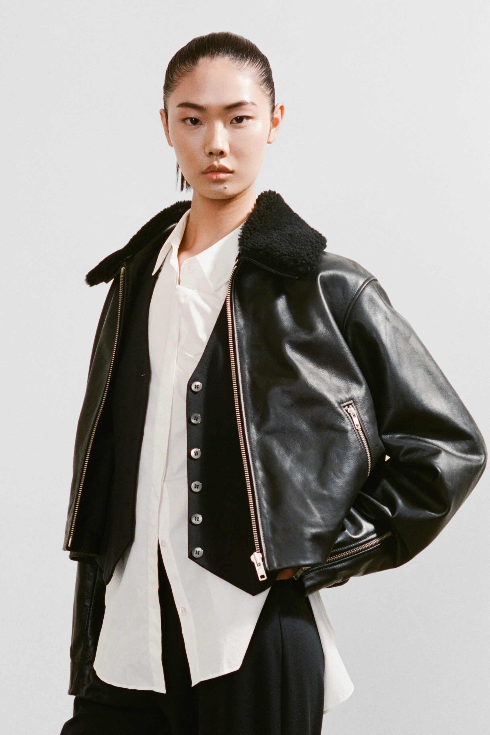 A fitted black leather jacket paired with a white collared shirt, featuring a zippered detail.