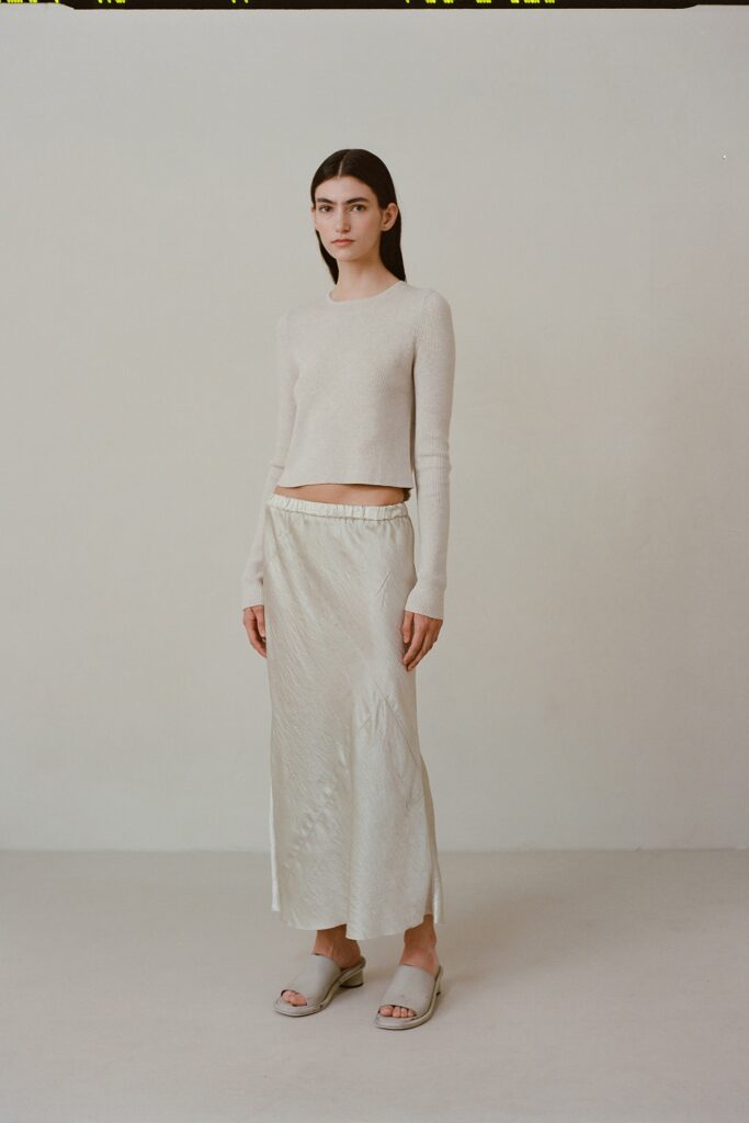 A fitted beige silk long-sleeve top paired with a cream skirt featuring a slit detail.