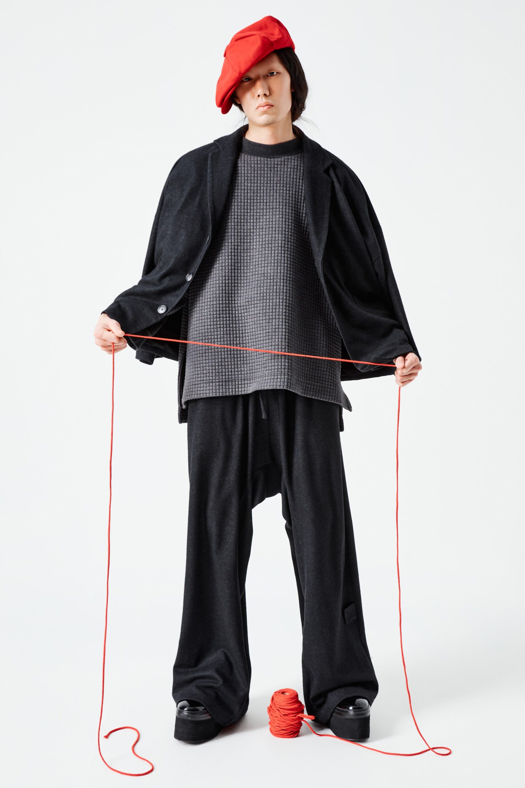 This ensemble features a relaxed black wool jacket with a collared design, layered over a textured top. The wide-leg pants create a flowing silhouette that enhances movement, while the overall monochromatic palette offers a striking visual impact.