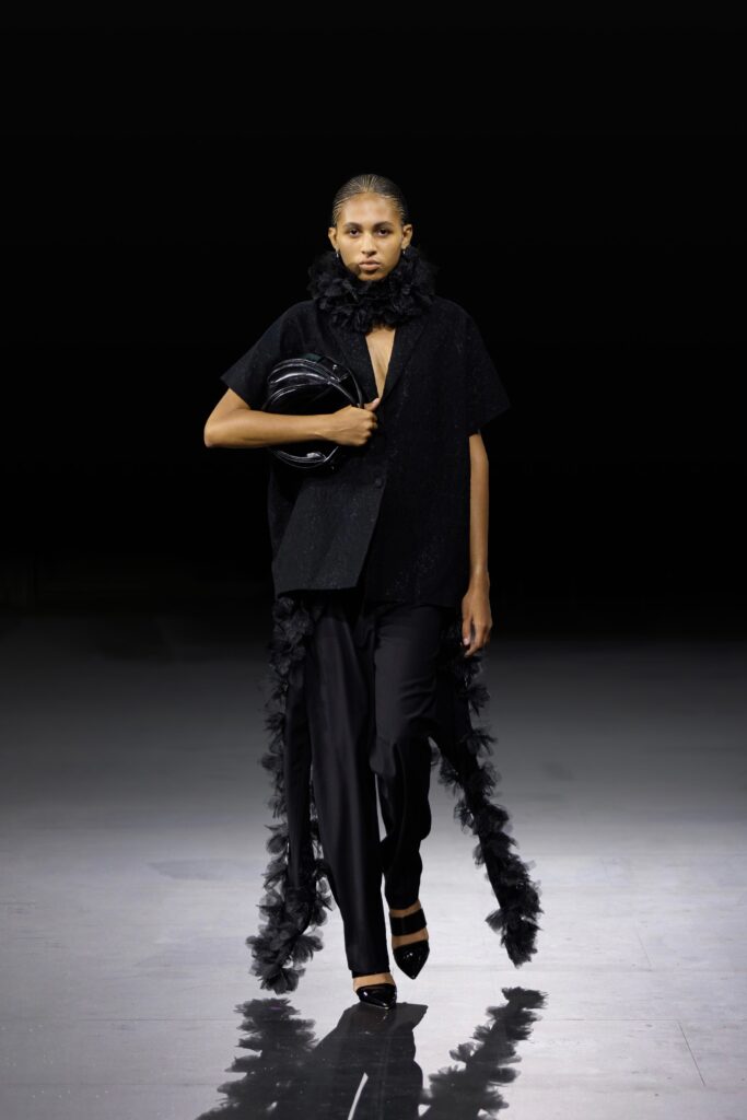 An elegant black asymmetric silk top paired with tailored black pants featuring layered detailing.