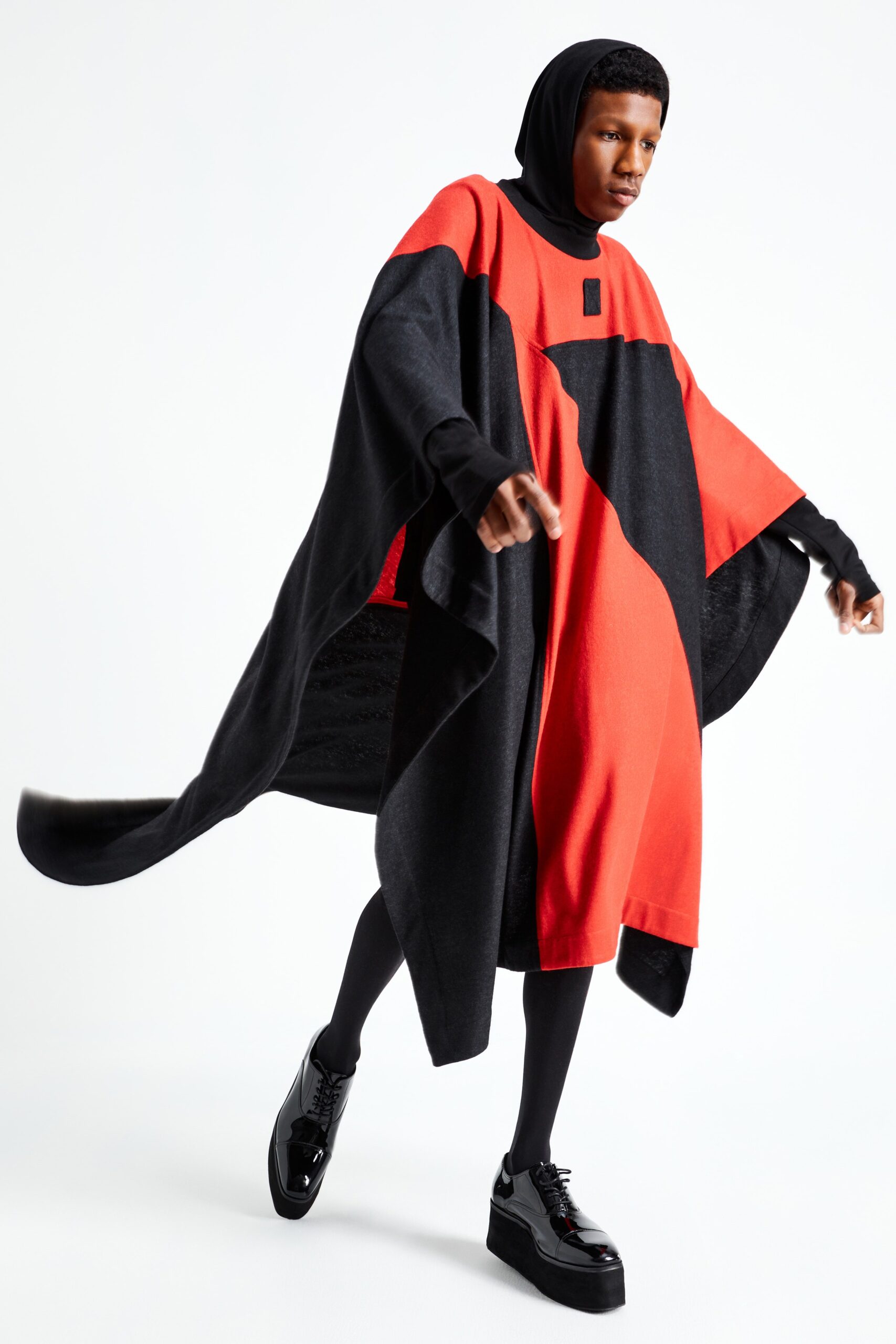 This oversized poncho features a striking interplay of black and red, creating a bold visual statement. The high-neck design adds an element of structure, while the asymmetric cut enhances movement and fluidity, making it a standout piece in any collection.