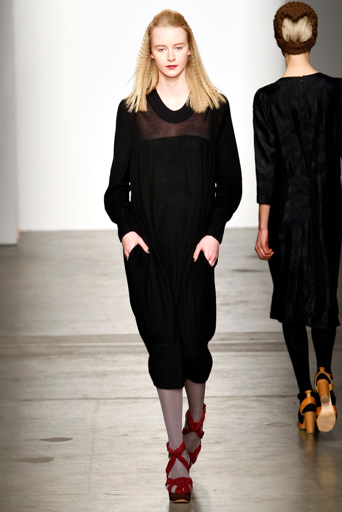 A relaxed black cotton dress with long sleeves and a V-neckline featuring layered design details.