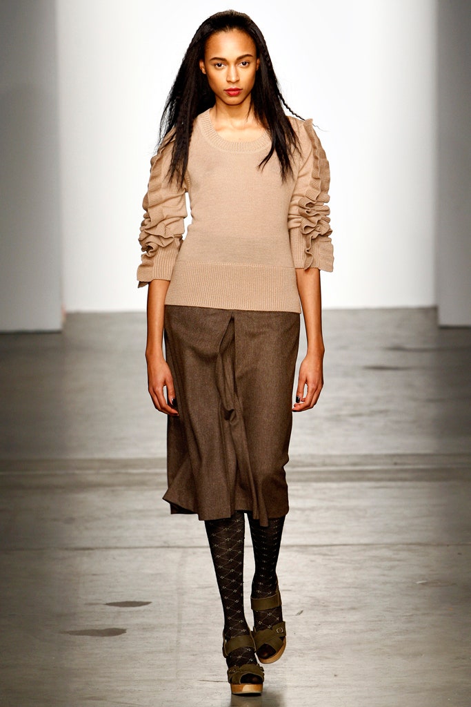 A fitted beige top with long sleeves paired with a pleated brown skirt.