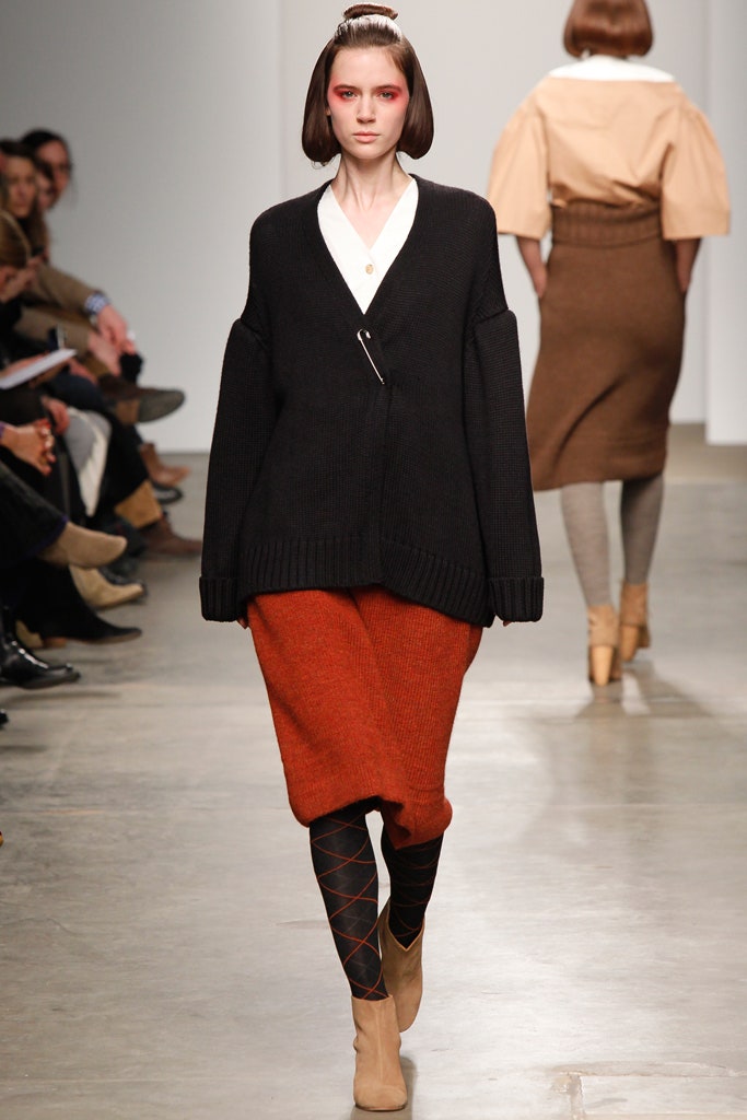 An oversized black sweater paired with a layered orange skirt, featuring a collared neckline.