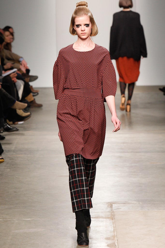 A relaxed red checked dress paired with black pants featuring an asymmetric design.