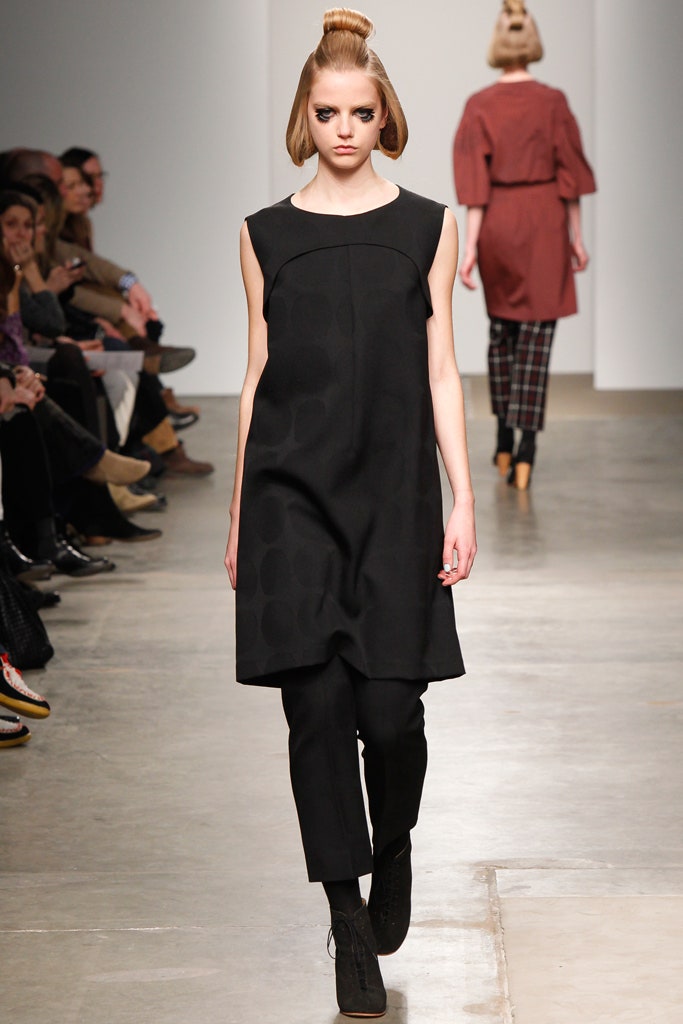 A relaxed black sleeveless dress paired with straight-leg pants for a modern look.