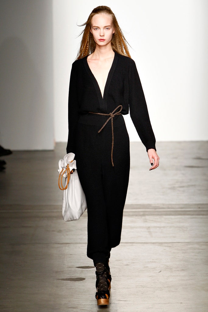 A fitted black cotton jumpsuit with long sleeves and a V-neckline, featuring a belted waist.