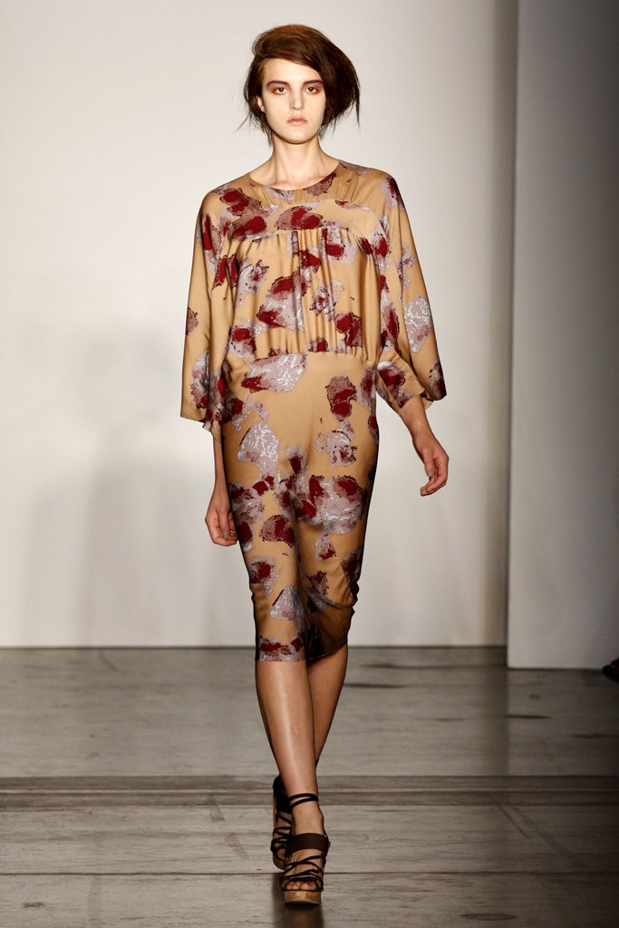 A fitted beige dress with floral patterns and a V-neckline, featuring long sleeves and pleated details.