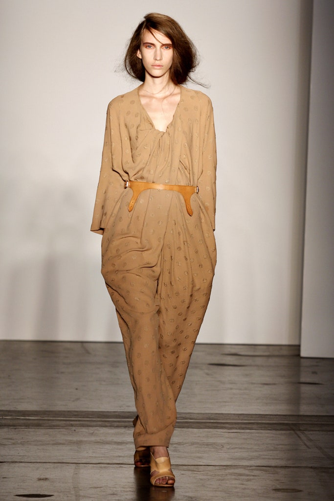 A relaxed beige jumpsuit with long sleeves, a V-neckline, and embroidered details.