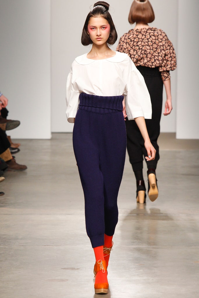 A fitted white collared top paired with high-waisted navy pants featuring pleated details.