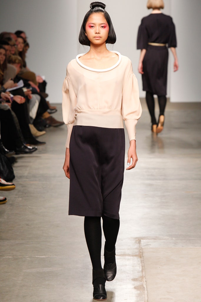 A fitted beige and navy dress with long sleeves and a collared neckline featuring an asymmetric design.