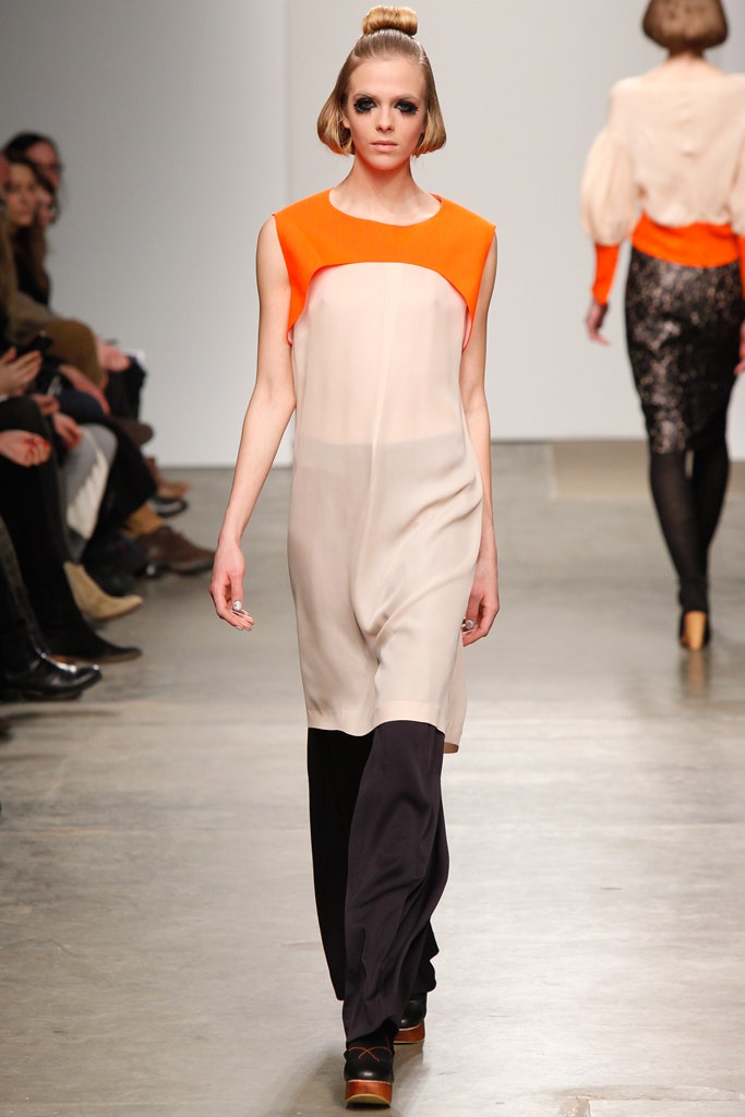 A relaxed sleeveless dress featuring a high-neck and asymmetric design in beige, black, and orange.