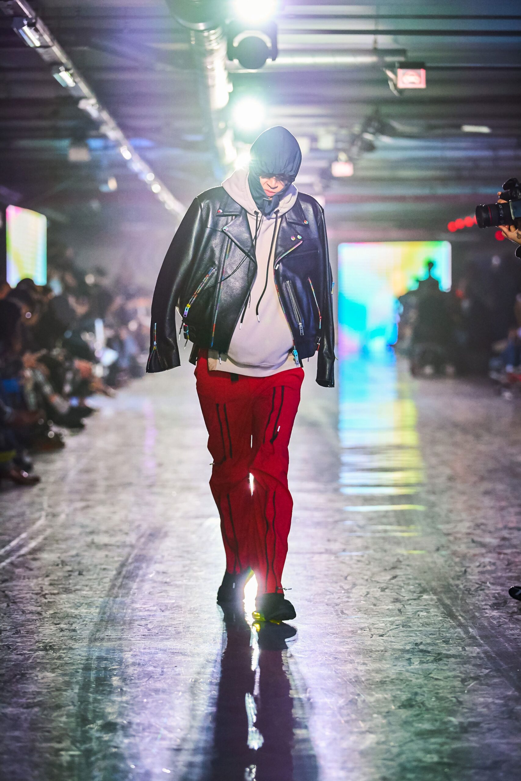 A relaxed black leather jacket with a hood paired with red printed pants.