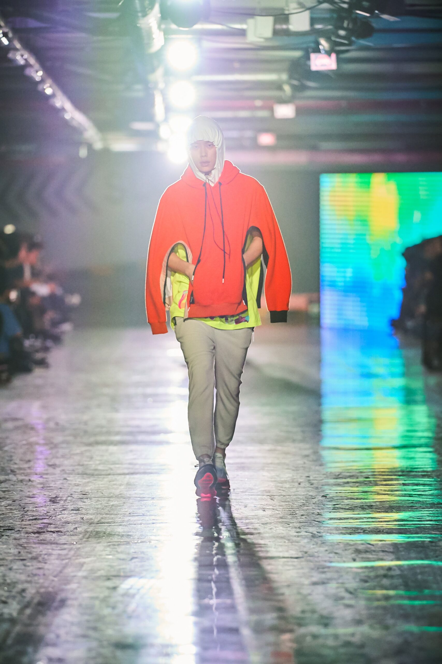 A relaxed orange hoodie paired with gray pants, featuring a layered look and hooded design.