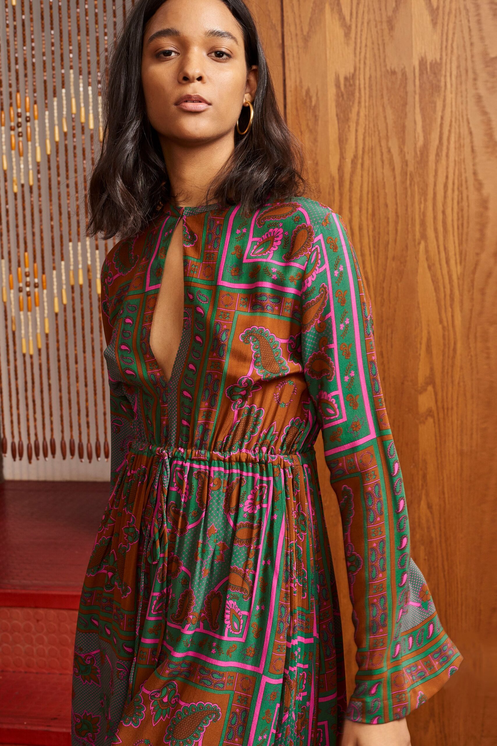 A relaxed brown dress with long sleeves, a V-neckline, and colorful printed patterns.