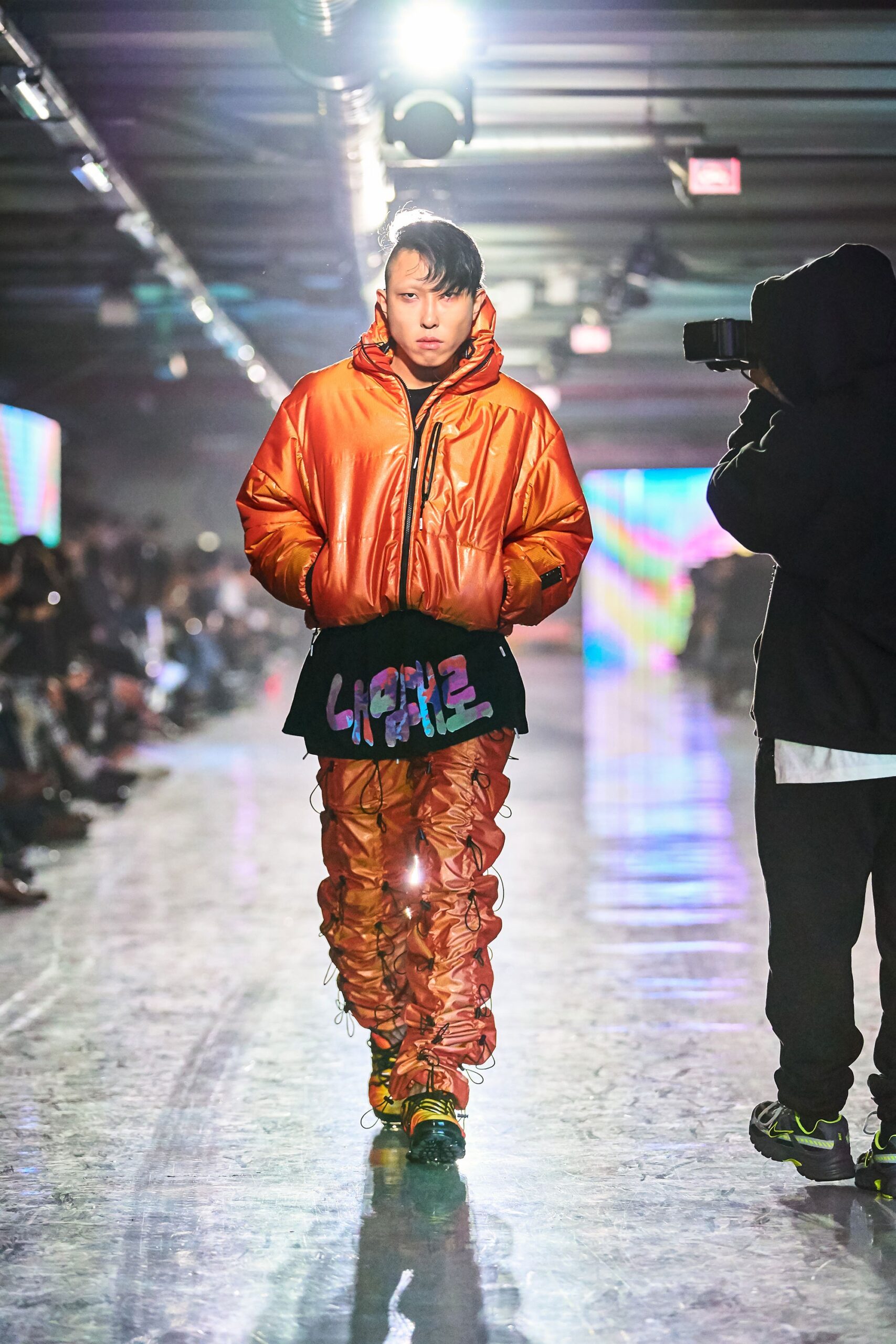 A relaxed-fit orange hooded jacket paired with layered black pants.