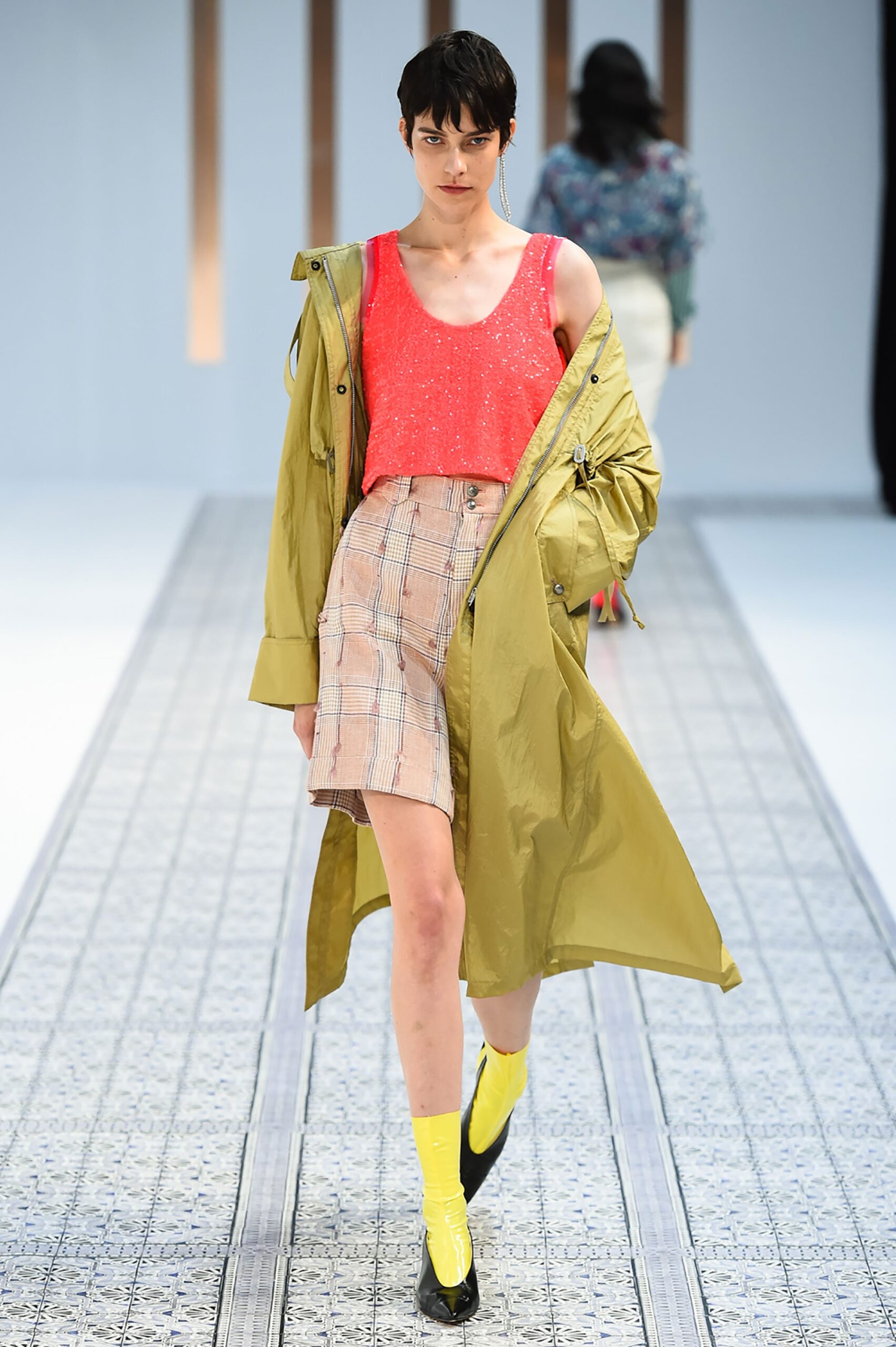 A relaxed yellow coat layered over a sleeveless pink top with checked shorts.