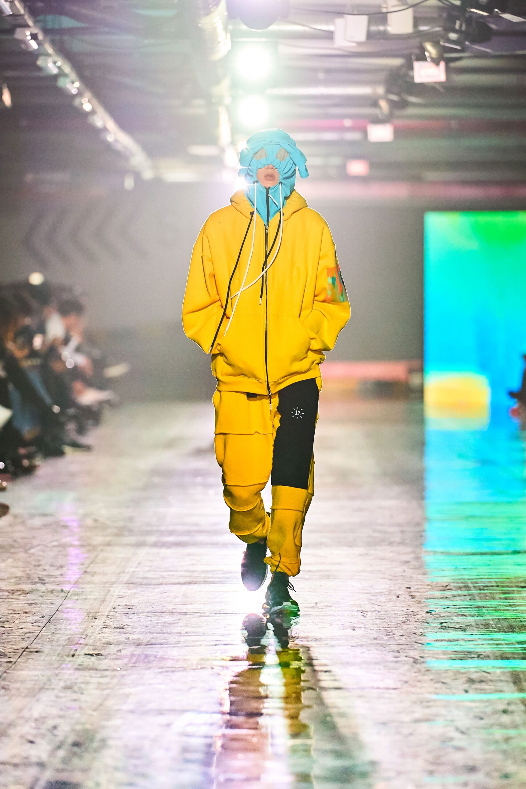 A relaxed yellow cotton hooded jacket paired with black pants featuring zippered details.