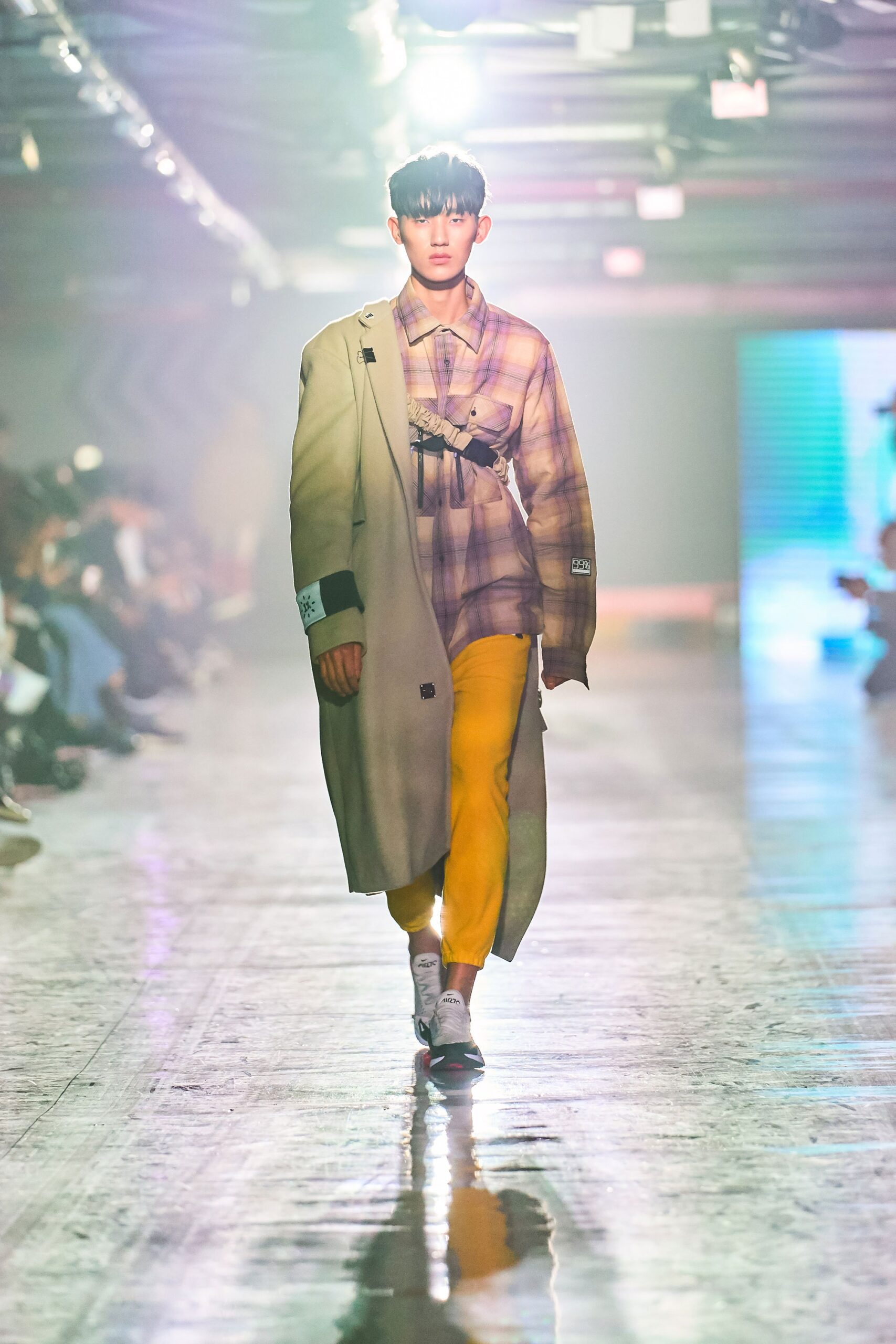 A relaxed beige coat layered over a long-sleeve checked shirt and yellow pants.