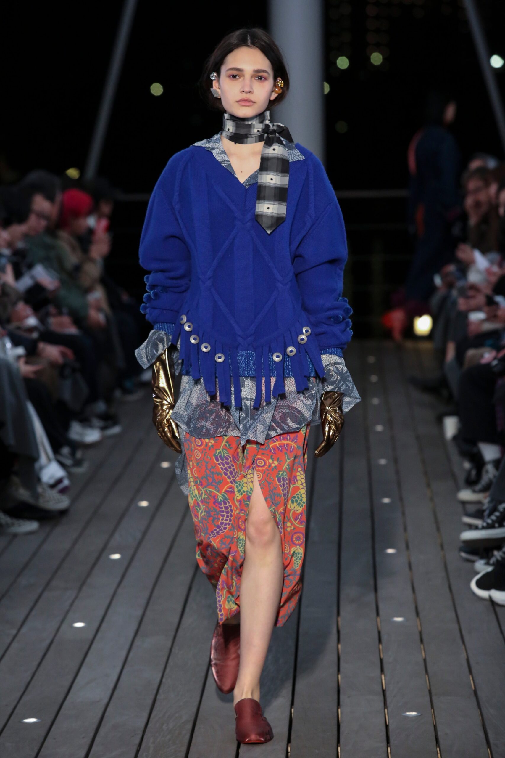 A relaxed blue long-sleeve sweater with fringed details paired with an asymmetric multicolor skirt.