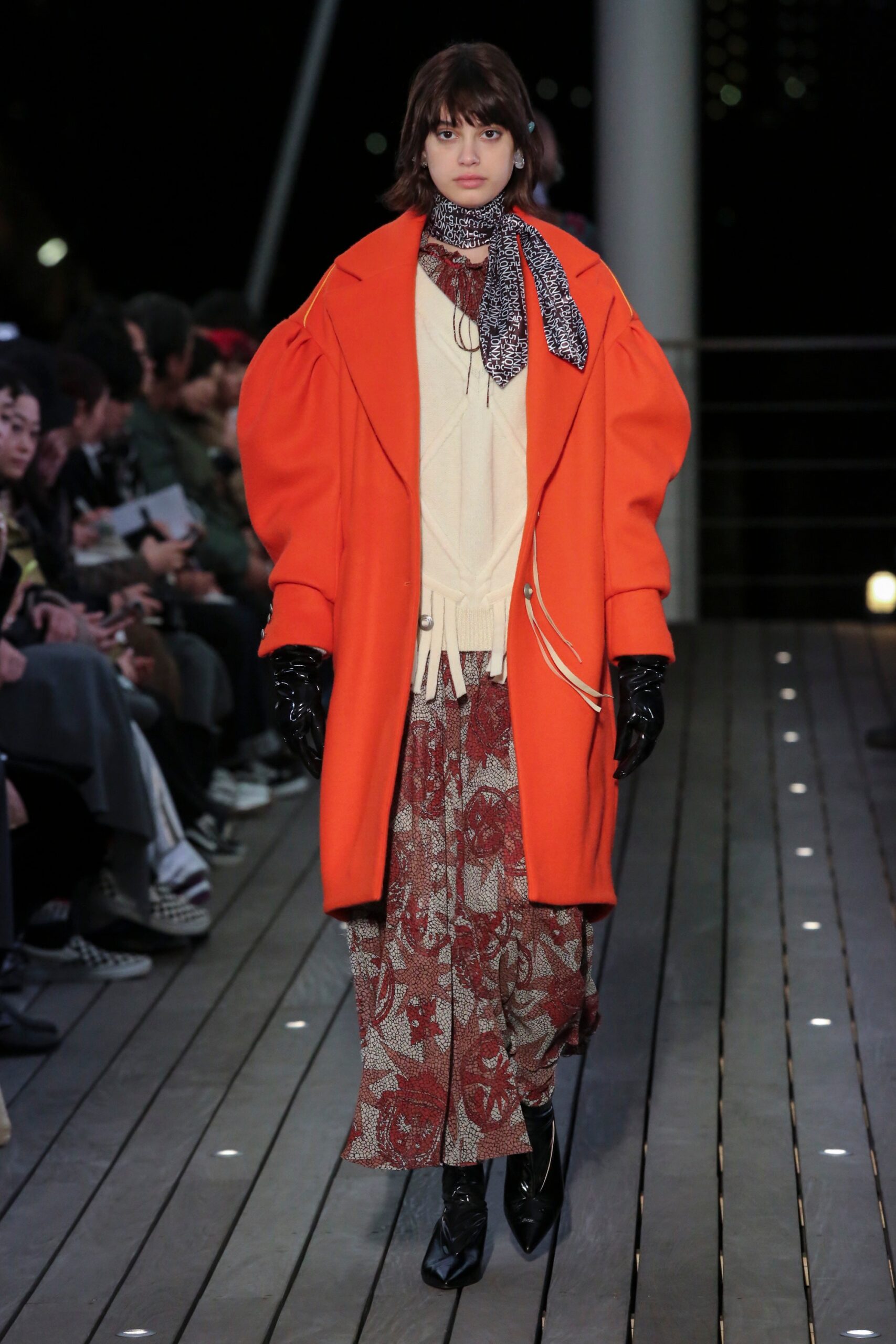 A relaxed orange coat layered over a printed dress with long sleeves and a collared neckline.