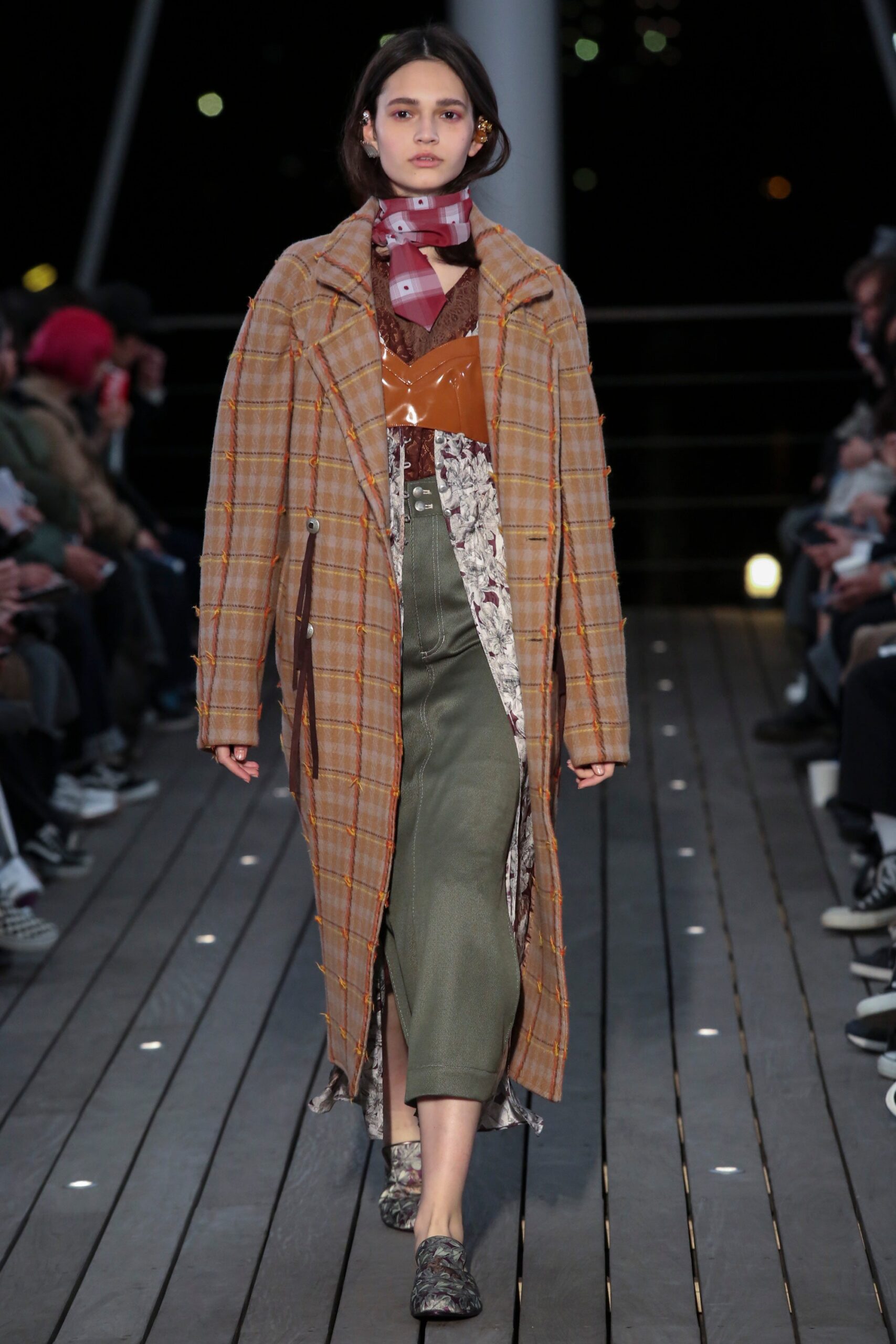 A relaxed brown plaid coat layered over a green dress with long sleeves and a collared design.